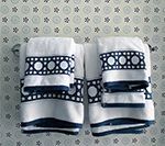 White towels with navy blue borders and circular patterns hang on a silver towel rack against a patterned wall.