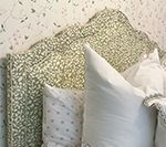 Pillows in varying sizes and patterns, including floral and dotted, on a bed, with wallpaper in the background.