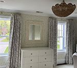 Bedroom with white dresser, mirror, floral curtains, and chandelier.