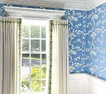 Room interior with blue floral wallpaper, white curtains framing a window, and white trim.