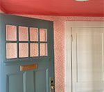 Blue front door with window panes, salmon-colored textured walls and ceiling, and a white door.
