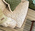 Cream-colored patterned armchair with throw pillows and a green blanket, beside striped rug.