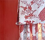 Red and white floral patterned curtain hanging in front of a solid red wall.