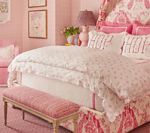 Pink bedroom with floral bedding, upholstered bench, and framed artwork.