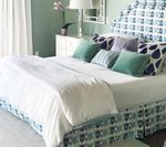 Bedroom with a white bed, patterned headboard, and blue-green accent pillows against a light green wall.