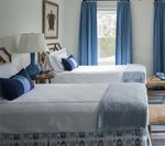 Two twin beds with white bedding, blue accents, blue curtains, and a framed turtle picture.