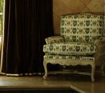 Armchair with patterned upholstery beside a dark curtain and window.