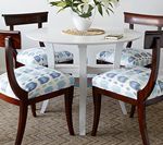 Round white table with four chairs, floral cushions, and a vase of flowers.