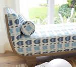 Blue patterned chaise lounge with bolster pillow near a window.