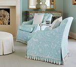 Two blue patterned armchairs in a living room, with a footstool and fireplace.