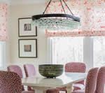 Dining room with pink chairs, white table, floral window shades, and a chandelier.