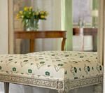Upholstered bench with patterned fabric. A table with flowers and a mirror reflection of a room are visible.