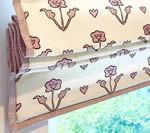 Cream-colored Roman shade with pink floral pattern and trim over a window.