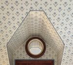 Ceiling with decorative wallpaper, circular window, and a wooden door frame.