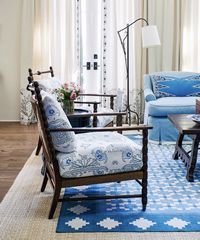 Living room with blue patterned furniture, rug, and cream-colored curtains.