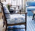 Wooden armchair with blue patterned cushion, light blue sofa in the background, blue patterned rug.