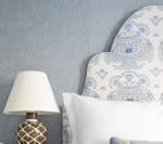 Bedside lamp on nightstand next to patterned headboard and white pillow, against a blue wall.