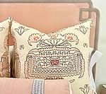 Cream and peach embroidered pillow on a peach headboard with a silver accent pillow.