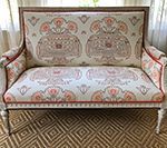 Upholstered loveseat with a floral patterned fabric, cream and coral, on a woven rug.