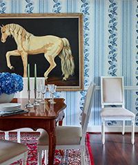 Dining room with a horse painting, blue patterned wallpaper, and a red rug.
