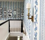 Stairwell with light blue and white striped wallpaper, black and white framed photos, and a gold sconce.