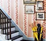 Staircase with floral wallpaper, framed art, and an umbrella stand holding yellow umbrellas.