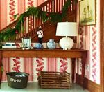 Wooden console table with lamp, garland, and basket on a staircase with red floral wallpaper.