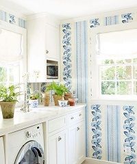 White and blue laundry room with washer, cabinetry, and floral wallpaper border.