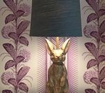 Rabbit-shaped lamp with black shade against purple floral wallpaper.