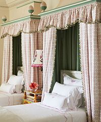 Two beds with pink floral canopies and white bedding, in a light-colored room.