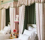 Two beds with pink canopy curtains and white bedding in a room.
