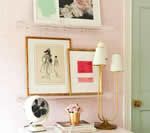 Pink-walled room with artwork and gold lamp on a white table. A white fan is on the table.