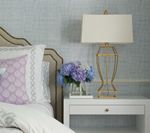 Bedside table with lamp, flowers, and pillows; light blue and gold tones.