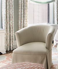 Beige upholstered armchair by a window with patterned curtains.
