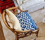 Wicker chair with blue and white patterned pillow and tan pillow, against rug and furniture.