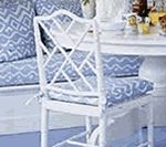 White lattice-back chair with patterned blue cushion next to a white table.