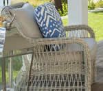 Wicker chair on a porch with beige and blue pillows, bright grass in background.