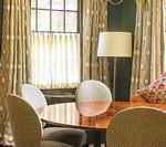 Dining room with round table, chairs, curtains, and a lamp. A decorative white and peach vase sits on the table.