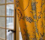Yellow curtain with floral design partially obscuring a window with a blurred view of a building.