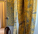 Yellow curtains with a blue floral pattern hang over a doorway. A wooden chair is in the foreground.