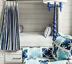 Blue and white nautical-themed bunk bed and couch. Striped curtains, blue lamp, patterned pillows, white shiplap walls.