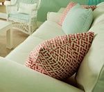 White sofa with patterned red and blue pillows, near a wicker chair.