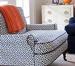 Armchair with black and white patterned fabric, orange blanket, chest of drawers.