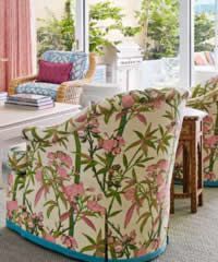 Floral upholstered chairs near a table, next to a window overlooking greenery.