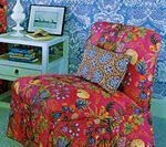 Chair with vibrant floral pattern, blue patterned pillow, and white nightstand with lamp and picture.