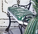 Black metal bench with green and white patterned cushion, set against a white wall with black dot design.