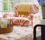 Armchair with orange and white patterned fabric, yellow throw, and a drink on a tray.