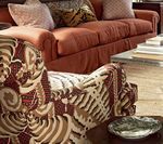 Living room with orange sofa, patterned armchair, and decorative pillows.