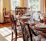 Dining room set for a meal; dark wood chairs and table, set with plates and glasses near a window.