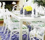 White dining table and chairs, tropical-print cushions, yellow flowers, blue patterned rug.